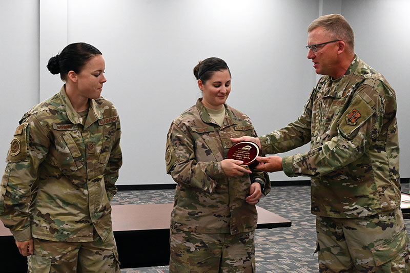 Chief Master Sgt. Jeff Miller, the North Dakota Air National Guard state command chief, presents the N.D. Air National Guard family of the year award to Staff Sgt. Sarah Harper as her wife Staff Sgt. Jessica Harper, both of the 219th Security Forces Squadron, looks on at Minot Air Force Base, Minot, N.D., on July 18, 2020. (U.S. Air National Guard photo by Chief Master Sgt. David H. Lipp)